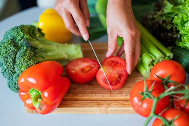 girl cook in the kitchen cuts a tomato with vegetables with a knife