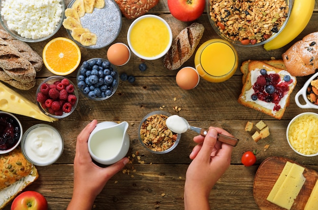 Girl cooking breakfast - granola with yogurt, fruits, berries, milk, yogurt, juice, cheese. Clean eating, dieting, detox, vegetarian food concept.