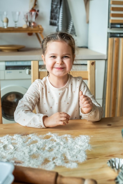 Girl cooks at home in a bright kitchen a child stirs flour on the table baby helps mom and laughs