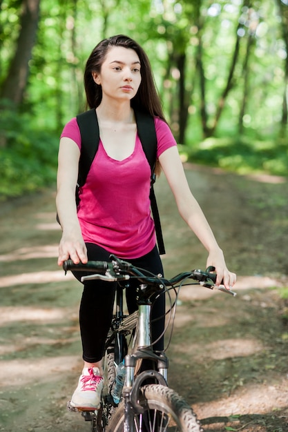 Girl cyclist in pink t-shirt on a bike on asphalt road in the forest