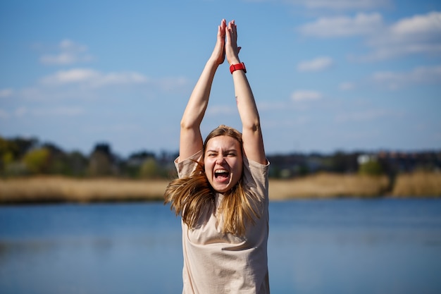 Girl dancing near the lake, sunny weather. A young woman rejoices in life, dances and sings. She has a good mood and a smile on her face.