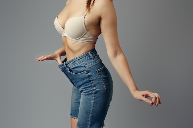 Photo the girl demonstrates that her jeans have become big closeup on a gray background weight loss concept