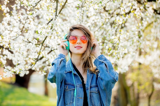 girl in a denim jacket and headphones near a flowering tree