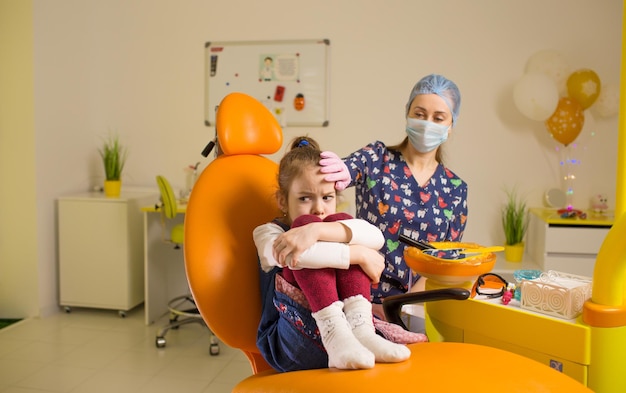 A girl dentist calms a frustrated little girl sitting in a dental chair at a doctor's appointment