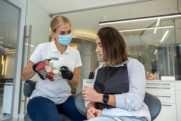 Girl dentist shows a model of jaws as a visual aid to a girl patient A sample of jaws for training dentists teaches how to care for teeth Dental health Female dentist