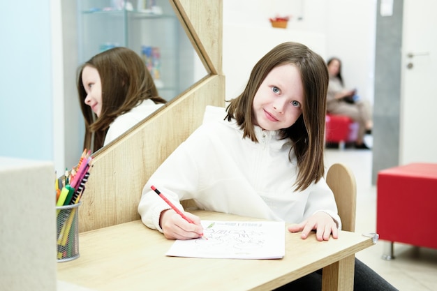 A girl in dentistry draws with pencils while waiting for her mother