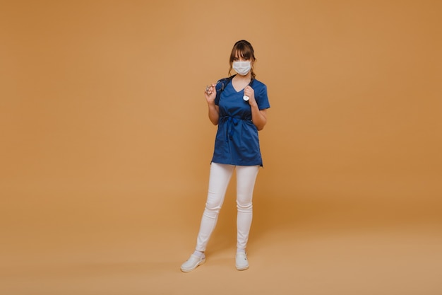 A girl doctor stands in a medical mask, isolated on a gray background.