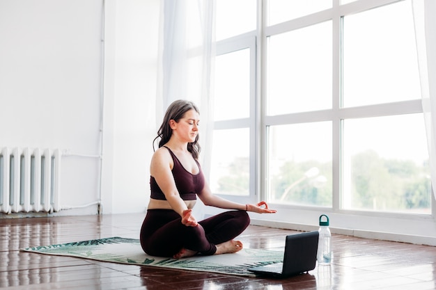 Girl does exercises, stretching, yoga, mat near the window, yoga suit, body, slimness and health, exercises via the Internet, remote classes, computer trainer