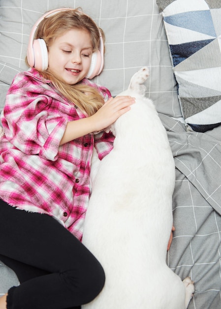 Girl and dog laying on couch in headphones, listening to music with her smarthphone.