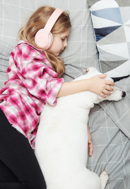 Girl and dog laying on couch in headphones, listening to music with her smarthphone.