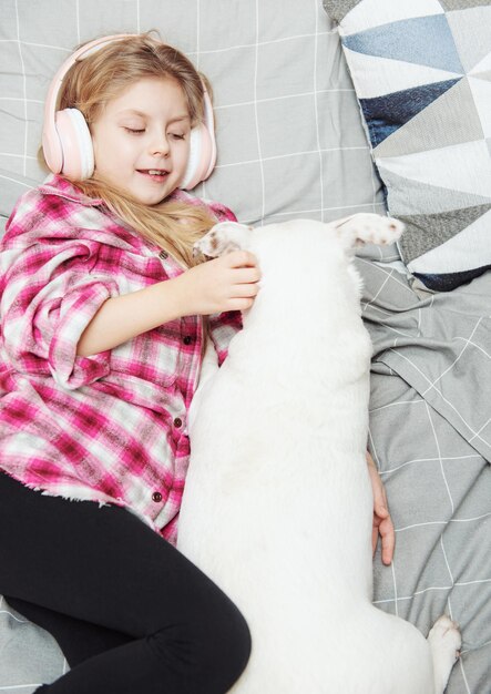 Girl and dog laying on couch in headphones, listening to music with her smarthphone.