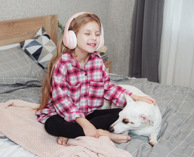 Girl and dog sitting on couch in headphones, listening to music with her smarthphone.