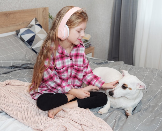 Girl and dog sitting on couch in headphones listening to music with her smarthphone