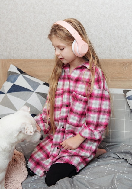 Girl and dog sitting on couch in headphones listening to music with her smarthphone