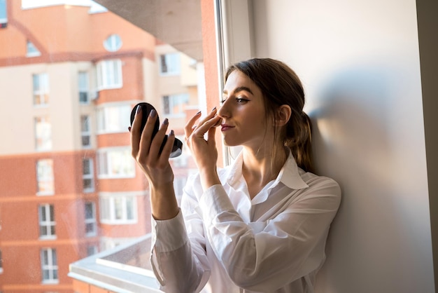 Girl doing itself makeup near window in the background before taking a photossesion