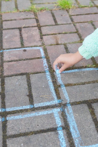 Girl draws a hopscotch with chalk on the pavementChild playing the game outside Kid wearing sweater during playing hopscotch Activities for childrenchild paintings on asphalt