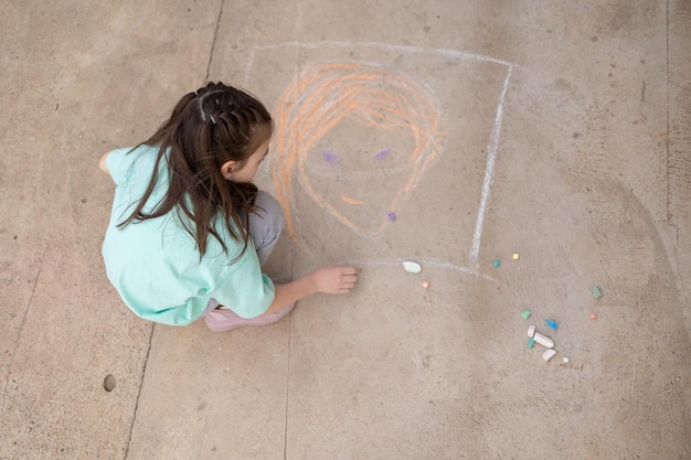 Girl draws with colorful crayons on pavement Children39s drawings with chalk on wall Creative kid Joy of childhood