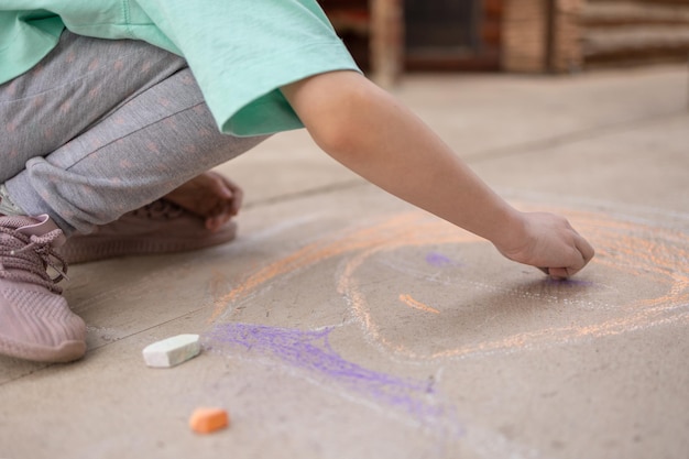 Girl draws with colorful crayons on pavement Children39s drawings with chalk on wall Creative kid Joy of childhood