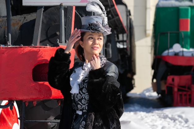 Girl dressed as a noblewoman of the 19th century near a steam locomotive. Russian winter