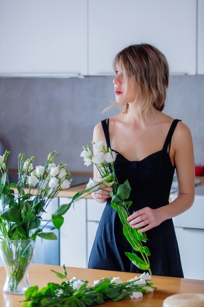 A girl dressed in a black dress is holding white roses in a bouquet before putting them in a vase. Sprint time concept