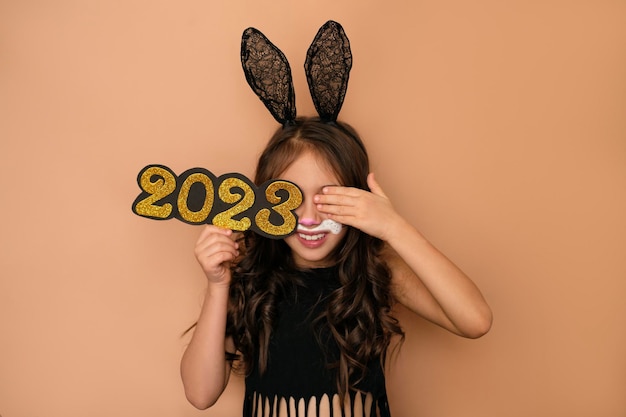 Girl dressed up as rabbit holds number of new year 2023 and closes eye with hand