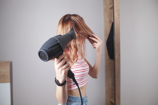 Photo girl drying hair with hairdryer in home.