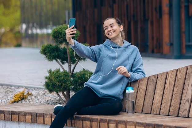 Girl in earphones taking selfie outdoors bending head