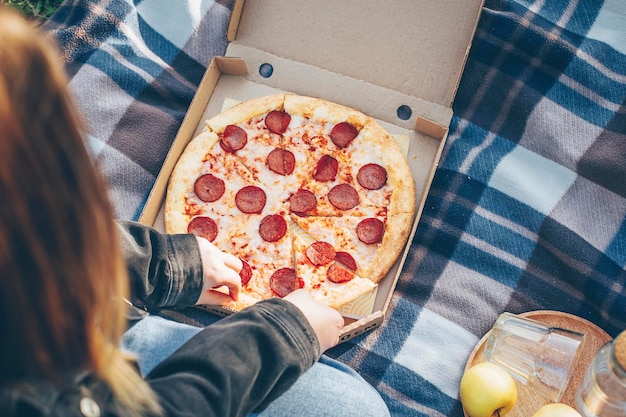 Girl eating tasty pepperoni pizza while sitting in nature at a picnic