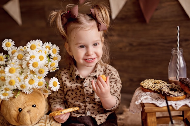 The girl eats cookies and feeds them with a teddy bear.