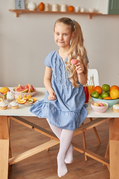 Girl eats sweet macaron at the kitchen