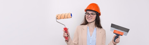 Girl engineer in an orange construction helmet with plastering painting tools in her hands on a white background