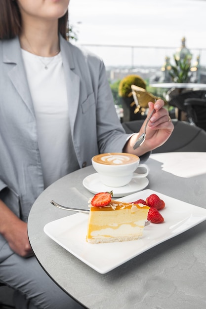 Girl enjoy classic cheesecake with fresh strawberry with cup of coffee on white table. Close Up view. Tasty breakfast. Piece of cake on plate, white cup on white marble background.