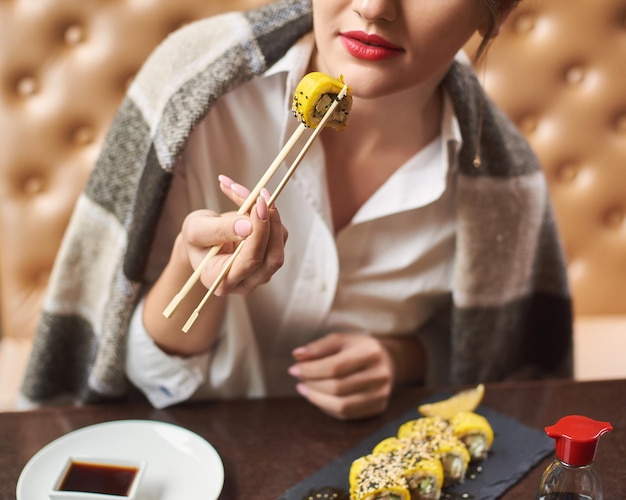 Girl enjoying asian dish with soy sauce using food sticks.