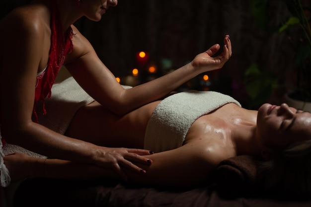 Girl enjoying therapeutic massage with oil in spa with dark lighting, closeup