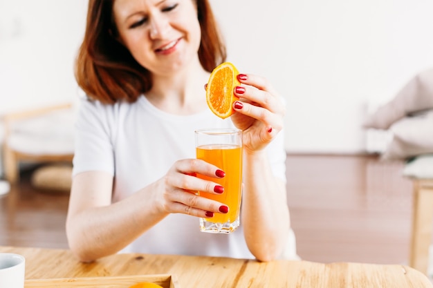 A girl of European appearance sits at a table in a white T-shirt, oranges for making smoothies and juice, the benefits of vitamins, morning