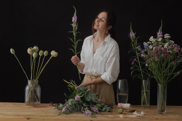 Girl florist collects a bouquet in a flower workshop on a dark background layout for floristry