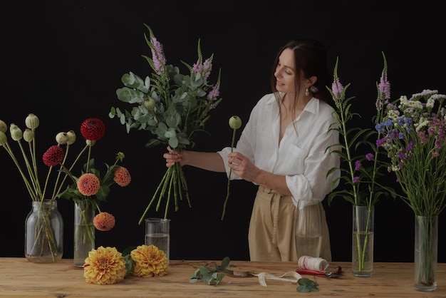 Girl florist collects a bouquet in a flower workshop on a dark background layout for floristry