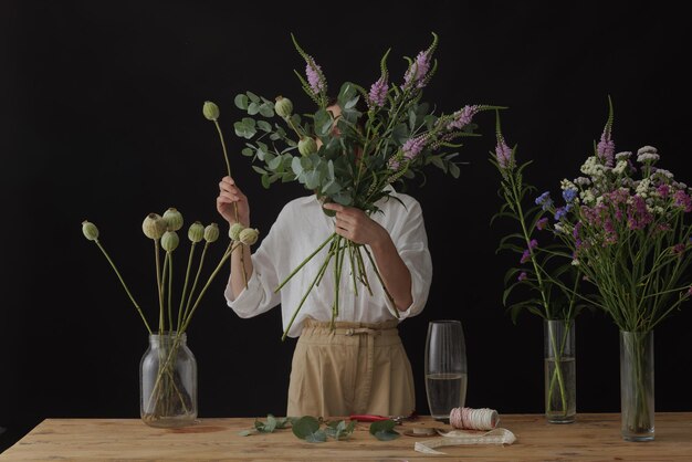 Girl florist collects a bouquet in a flower workshop on a dark background layout for floristry