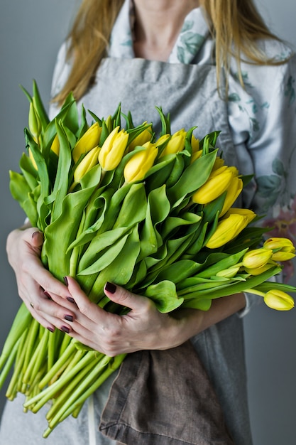 Girl florist holding a bunch of yellow tulips. Floristic. Gray background