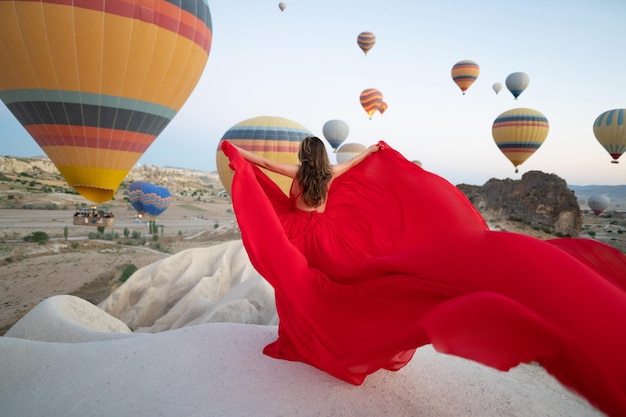 A girl in a flying dress with a long train on the background of balloons in Cappadocia