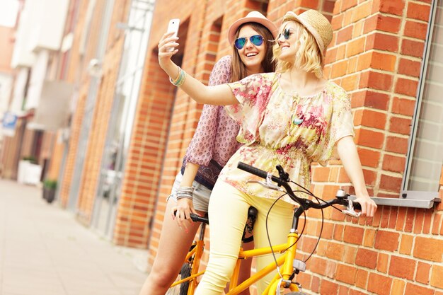 girl friends riding a tandem bicycle and taking selfie in the city