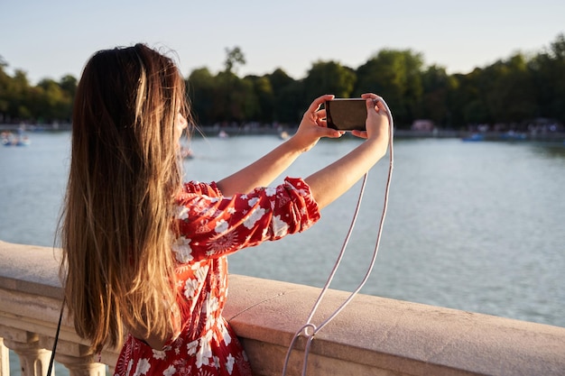 Girl from behind photographing with her smartphone on the lake