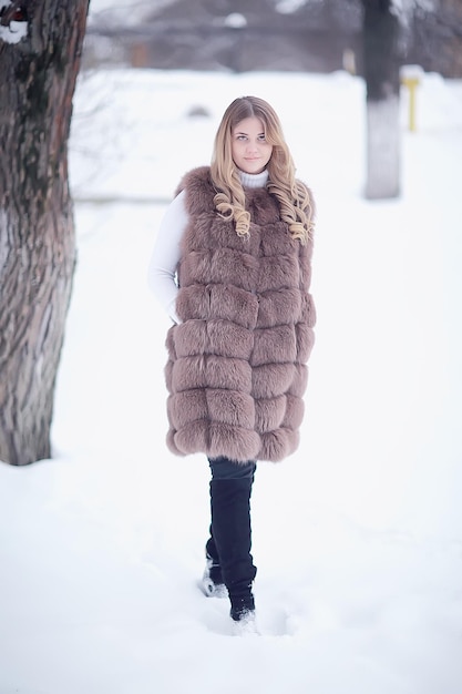 girl in a fur vest walks in the winter outside / adult young model in winter clothes fur