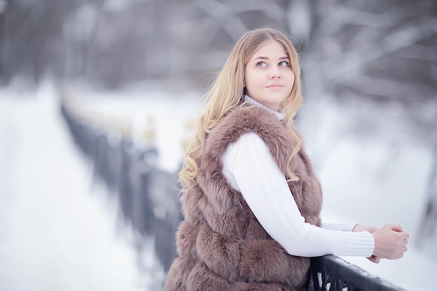 girl in a fur vest walks in the winter outside / adult young model in winter clothes fur