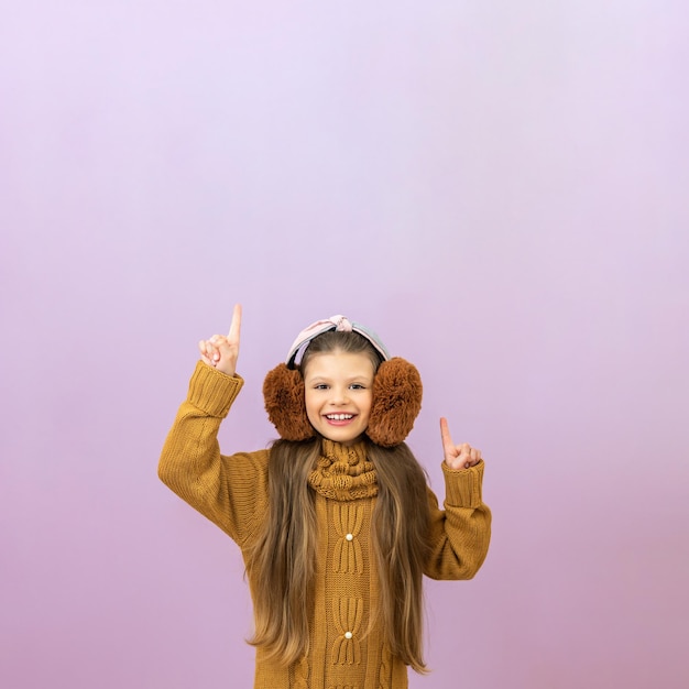 A girl in fur warm headphones on an isolated background a child in a warm sweater and ear muffs