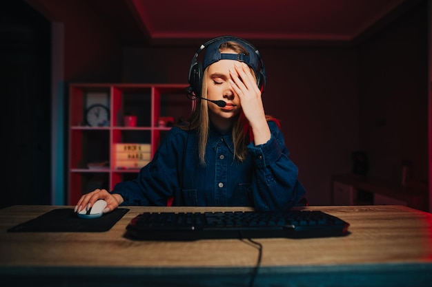 girl gamer sits at night at the computer and shows a gesture of facepalm lowered his eyes down