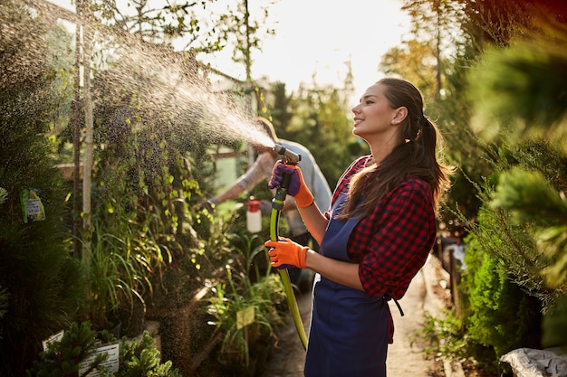 Girl gardener sprays water plants in the beautiful nursery-garden on a sunny day. Working in the garden .