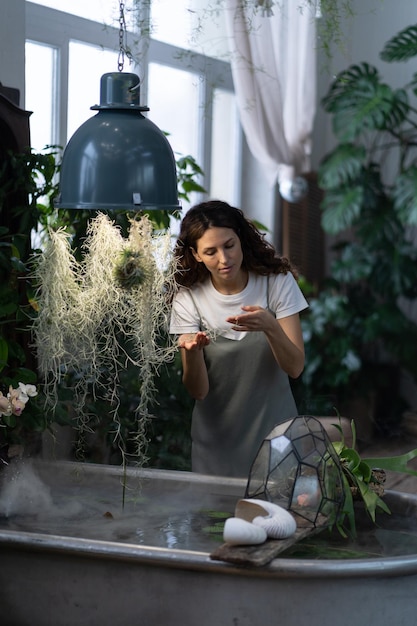 Girl gardener taking care about aquatic plant in greenhouse holding houseplant under bath with water