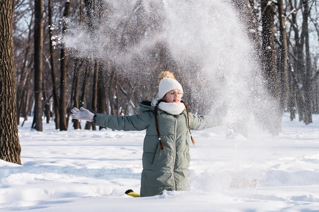 A girl in glasses and in warm clothes plays with snow in a winter park Walks in the air