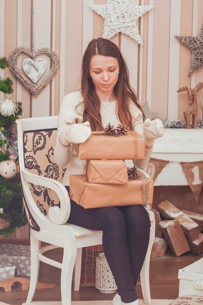 Girl in gloves holding gift boxes on her knees near Christmas tree